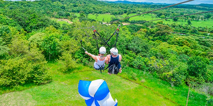 Duas pessoas na tirolesa Nascente Azul descendo de frente para vista de árvores e montanhas da Serra da Bodoquena - o que fazer em Bonito de graça