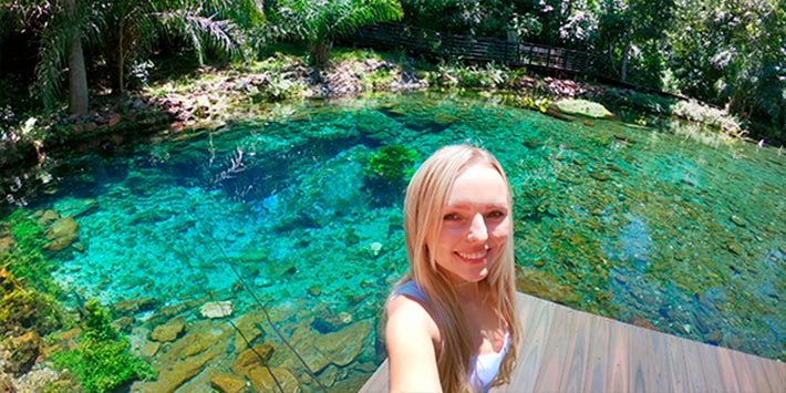 Selfie de mulher em meio à fauna e flora de Bonito MS - Nascente Azul - água cristalina com efeito natural em azul-turquesa e rica vegetação nativa ao redor.