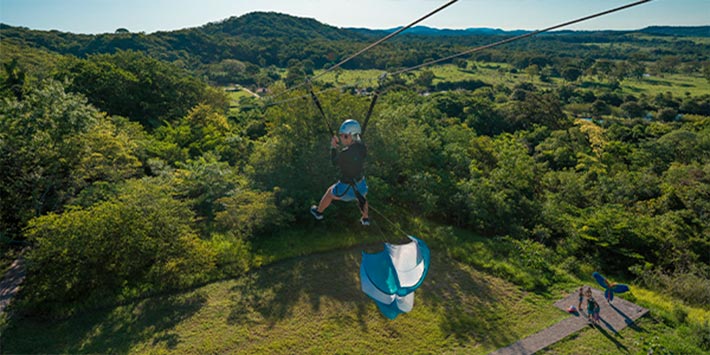Pessoa descendo tirolesa passando por árvores e vista da Serra da Bodoquena - Adventure Nascente Azul