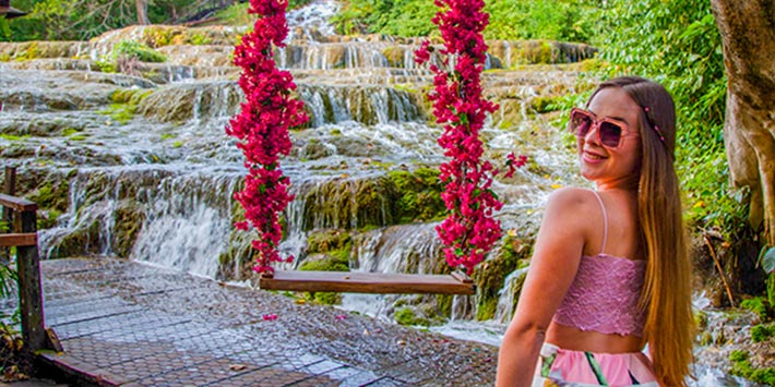 Mulher fazendo “selfie” no balanço de flores com vista para cachoeiras de tufas calcárias que deságua em forma de véu