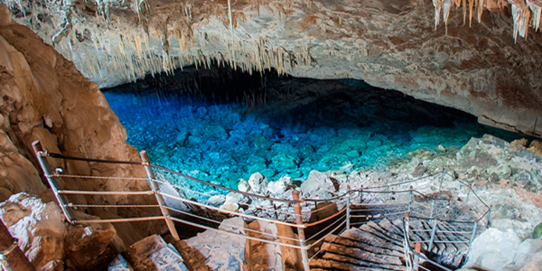 Imagem de gruta branca com formações rochosas pontudas e um lago azul no centro. 