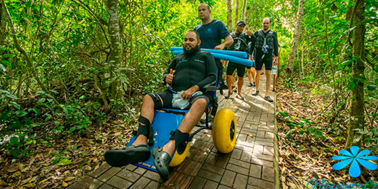 Grupo de turistas passando por trilhas acessíveis, como cadeirante em ênfase, mostrando a acessibilidade do passeio de flutuação
